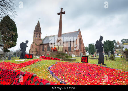 Knitted & crocheted red poppies on display together with standing soldier silhouettes, outside in UK churchyard, by war memorial. Armistice centenary. Stock Photo