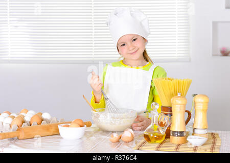 Cute little girl in chef's hat baking cake in the kitchen Stock Photo