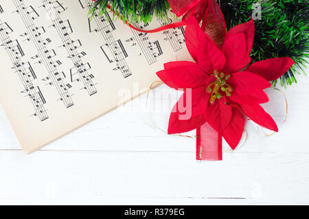 Christmas ornament and music sheet on white natural wooden table. Red ribbon bow. Poinsettia. Copy space at the bottom. Stock Photo