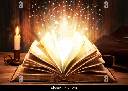 Old book with magic lights on wooden table by candlelight Stock Photo
