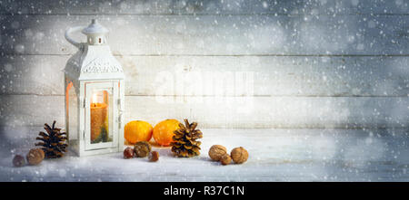 christmas decoration background with a candle light lantern, tangerines, cones and nuts in the snow on bright rustic wood, panoramic format with copy  Stock Photo