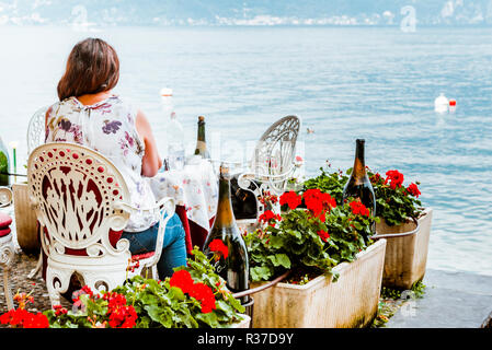 Woman sitting on the restaurant terrace facing the Como Lake. Varenna, Province of Lecco, Lombardy, Italy, Europe Stock Photo