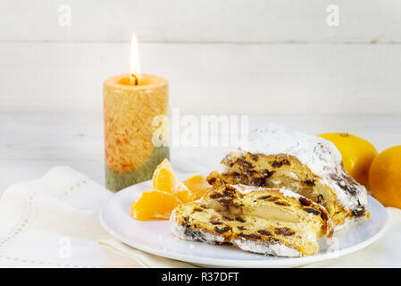 christmas cake, german christstollen with tangerines and a burning candle against a white wooden background with copy space, selected soft focus, narr Stock Photo