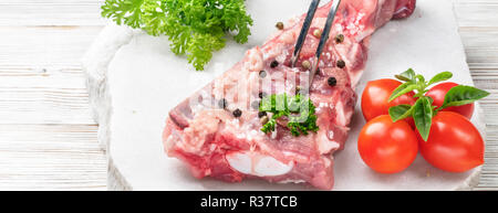 Fork in piece of meat pork brisket ribs spatula seasoned with salt and pepper cherry tomato and sprig of basil parsley on white wooden table marble st Stock Photo