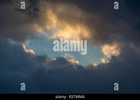 a hole in the clouds on a stormy day with an opening of blue sky within among the grey clouds. Stock Photo