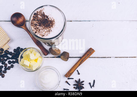 Bulletproof coffee. Ketogenic diet coffee with coconut oil and butter (ghee). Cup of bulletproof coffee and ingredients, paleo diet. On white wooden b Stock Photo