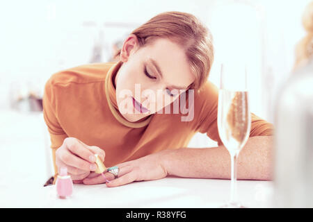 Pleasant short-haired ginger trans male carefully covering nails Stock Photo