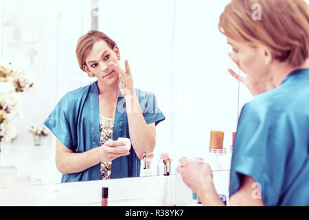Short-haired good-looking transgender applying night cream with his hands Stock Photo