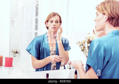 Calm short-haired young gender-queer applying full coverage foundation Stock Photo