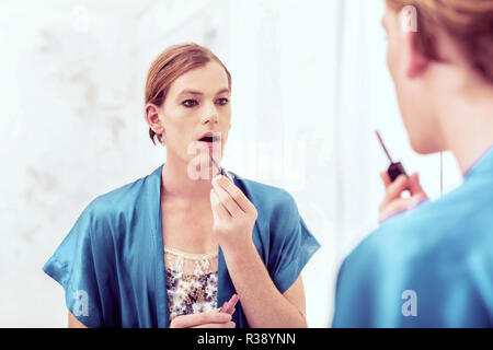 Short-haired travesty man covering his male face with cosmetics Stock Photo