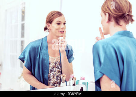 Smiling short-haired transgender gesturing to himself in mirror Stock Photo