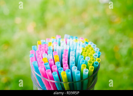 Bright colorful cocktail beverage straws and tubes put together in the big glass on green grass summer background. Preparing to the party Stock Photo
