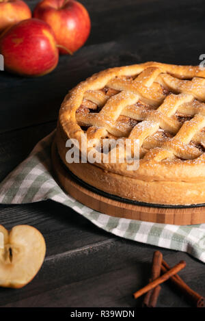 Homemade delicious apple pie with cinnamon and powdered sugar, on a kitchen towel, on a rustic table and apple fruits. Ready to eat sweet food. Stock Photo