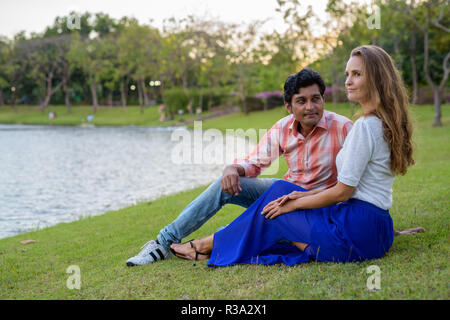 Multi ethnic couple thinking while sitting in the meadow against Stock Photo