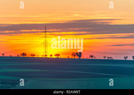 sun setting behind electricity pylon Stock Photo