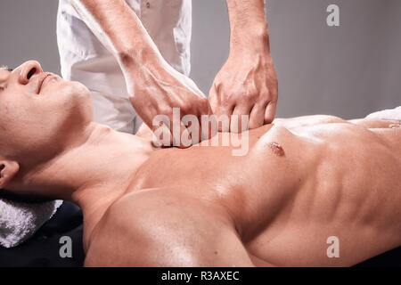 side view, two young man, 20-29 years old, sports physiotherapy indoors in studio, photo shoot. Masseur massaging athlete mans chest, muscular body, h Stock Photo