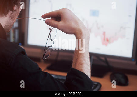 Analyzing data. Close up of a young businessman who holds glasses and looks at the gff while working in a creative office Stock Photo