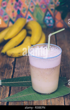 Banana smoothie (banana milkshake) on a wooden background with a bunch of bananas and green leaves. Healthy food concept Stock Photo
