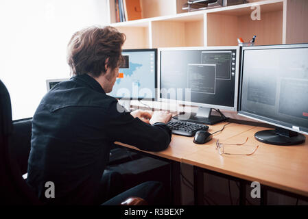 The young dangerous hacker breaks down government services by downloading sensitive data and activating viruses. A man uses a laptop computer with many monitors Stock Photo