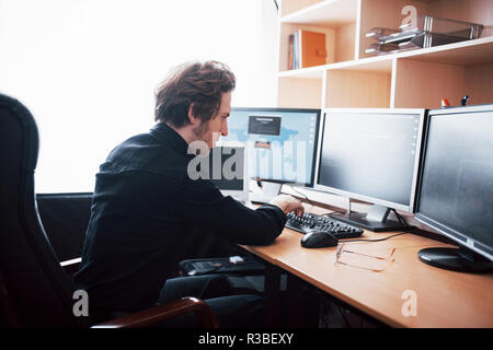 The young dangerous hacker breaks down government services by downloading sensitive data and activating viruses. A man uses a laptop computer with many monitors Stock Photo