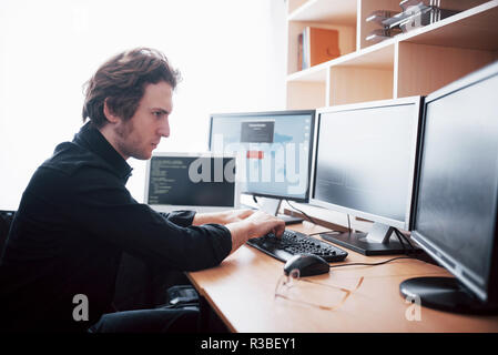 The young dangerous hacker breaks down government services by downloading sensitive data and activating viruses. A man uses a laptop computer with many monitors Stock Photo