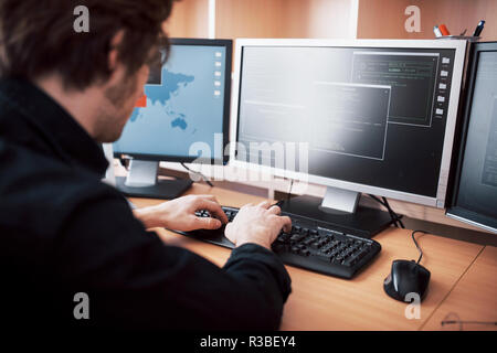The young dangerous hacker breaks down government services by downloading sensitive data and activating viruses. A man uses a laptop computer with many monitors Stock Photo
