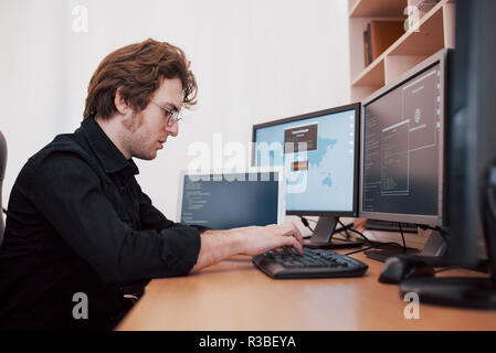 The young dangerous hacker breaks down government services by downloading sensitive data and activating viruses. A man uses a laptop computer with many monitors Stock Photo