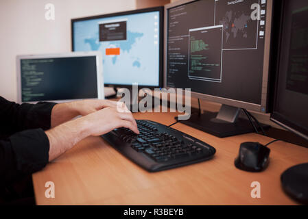 The young dangerous hacker breaks down government services by downloading sensitive data and activating viruses. A man uses a laptop computer with many monitors Stock Photo