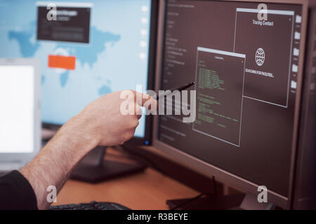 The young dangerous hacker breaks down government services by downloading sensitive data and activating viruses. A man uses a laptop computer with many monitors Stock Photo
