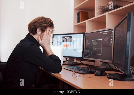 The young dangerous hacker breaks down government services by downloading sensitive data and activating viruses. A man uses a laptop computer with many monitors Stock Photo