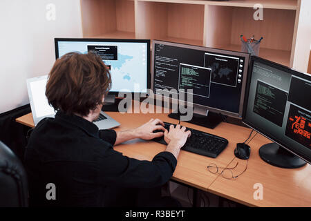 The young dangerous hacker breaks down government services by downloading sensitive data and activating viruses. A man uses a laptop computer with many monitors Stock Photo
