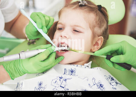 Hands of unrecognizable pediatric dentist and assistant making examination procedure for smiling cute little girl sitting on chair in hospital Stock Photo