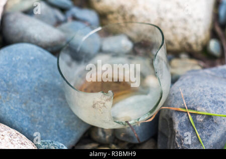A weathered broken glass jar left on stones by the river in the wilderness Stock Photo