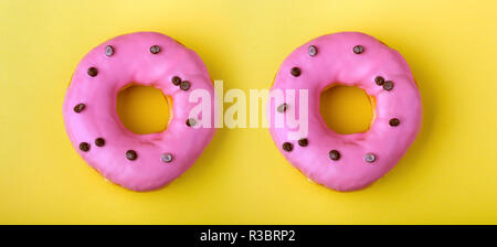 two donuts with pink icing on a yellow background Stock Photo