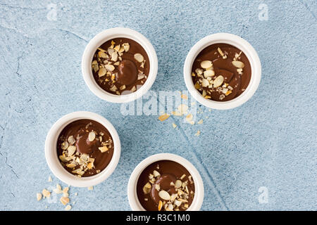 Ramekins filled with homemade chocolate pudding, decorated with roasted almond slivers, on light blue concrete background with copy space. Top view. Stock Photo