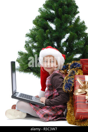 Little girl in Santa Claus cap with a laptop and Christmas gifts on white background, isolated Stock Photo