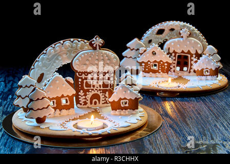 Christmas gingerbread house with a burning candle on a dark wooden surface against a black background. Stock Photo