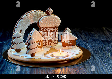 Christmas gingerbread house with a burning candle on a dark wooden surface against a black background. Stock Photo