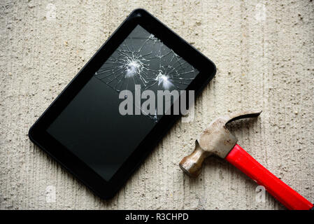 Broken tablet screen with red rusty hammer near it on concrete background Stock Photo