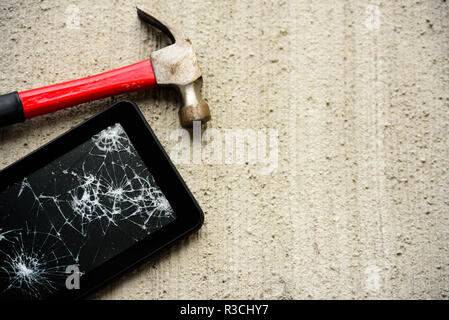 Broken tablet screen with red rusty hammer near it on concrete background Stock Photo