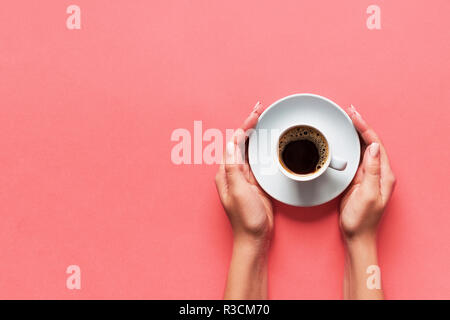 Minimalistic style woman hand holding a cup of coffee on pink background. Flat lay, top view. Stock Photo