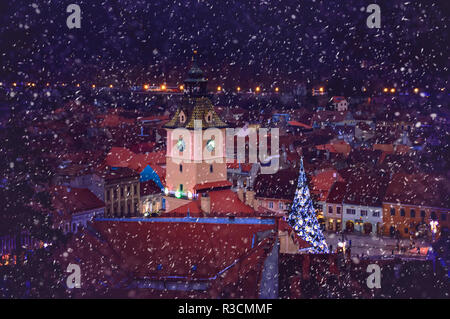 The City hall building and Christmas tree in the center of Brasov, seen from a distance through dancing snowflakes on a winter night. Stock Photo