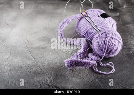 Hanks of woolen lilac threads, knitting needles and a knitting pattern on gray background Stock Photo