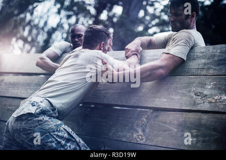 Soldiers helping man to climb wooden wall Stock Photo