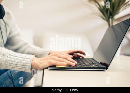 Woman working from home on laptop computer. Home office from a warm couch. Looking at screen. Focus on hands typing on a keyboard. Stock Photo