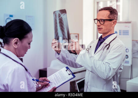 Making notes. Attentive young man checking results, staring at roentgen Stock Photo