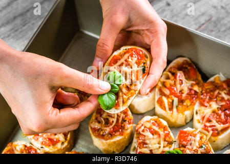 Chef in restaurant cooking italian food - bruschetta with baked tomatoes, basil and cheese, preparation appetizer for the party Stock Photo