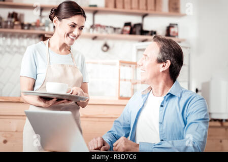 Professional waiter. Joyful pleasant woman smiling while serving coffee Stock Photo