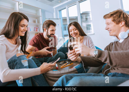 Finally meet. Low angle of positive four friends using gadgets and chatting Stock Photo