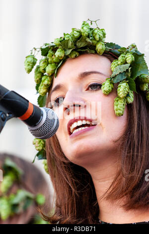 Faversham Hop Festival 2018, Blue Grass folk band Mockingbird. Close up. Caucasian woman singing into microphone while wearing hops around her head. Stock Photo